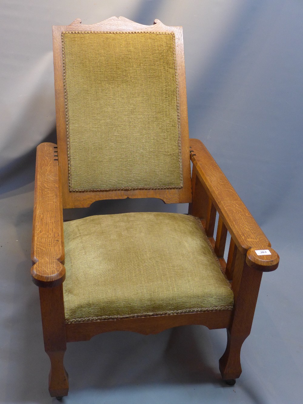 An arts and crafts oak reclining arm chair raised on tapered legs, spade feet and castors.