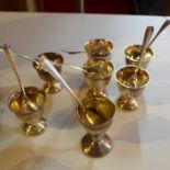 A set of six silver egg cups and matching spoons, together with one other.