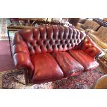 A 20th Century red leather hump back chesterfield three seater sofa raised on turned legs and