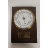 AN OAK CASED ANEROID BAROMETER, white enamel face. Brass presentation plaque of Montgomeryshire Con