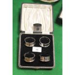 A CASED SET OF FOUR HALLMARKED SILVER NAPKIN RINGS, TOGETHER WITH ANOTHER