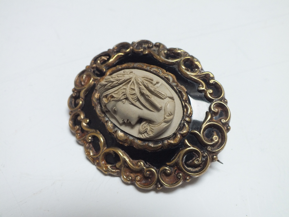 A VICTORIAN CARVED LAVA MEMORIAL BROOCH, of oval form with black enamel and scrolling yellow metal