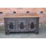 AN 18TH CENTURY OAK PANELLED COFFER, the triple panelled top above a carved triple panel front, arc