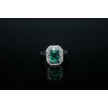 A HALLMARKED 18 CARAT WHITE GOLD EMERALD AND DIAMOND RING, the central emerald cut emerald of appr
