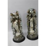 A PAIR OF CLASSICAL PLASTER FIGURES WITH NATURALISTIC BACKGROUNDS UNDER GLASS DOMES ON TURNED WOOD
