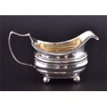 A George III silver cream jug, with gadrooned rim the rectangular ribbed body supported on four