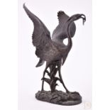 A late 19th century bronze model of a heron stood with wings outstretched, holding a fish in its