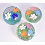 A circular domed glass paperweight decorated with multi-coloured flowers on a turquoise ground,