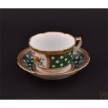 A 19th century Sevres porcelain cup and saucer painted with panels of flowers, on rich green