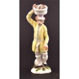 A rare 18th century Meissen model of a Russian fisherman stood holding a basket of fish on his head,