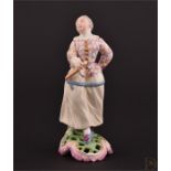 A rare 18th century Höchst porcelain figure of a harlequin lady wearing a colourful tunic, and stood