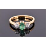 An 18 carat white gold, diamond, and emerald ring centred with an oval cut emerald, flanked by two