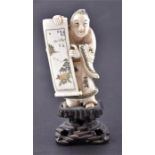 A Japanese Meiji period ivory figure holding an open scroll and wearing a floral kimono, on an