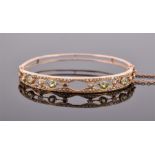 An Edwardian 9ct yellow gold, seed pearl and peridot bangle the openwork design set with seed pearls