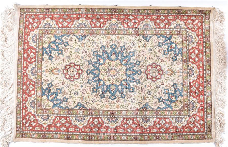 A Turkish Hereke silk rug  decorated with flowers on a cream ground, surrounded by red and green