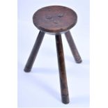 A simple small 18th century tripod stool  the circular dish seat in yew wood with incised border