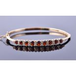 A 9ct yellow gold, diamond, and garnet hinged bangle set with nine graduated oval cut garnets,