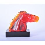 An amber tinted red glass car mascot in the form of a horse's head on a rectangular black glass