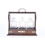 An early 20th century oak cased three bottle tantalus with three cut glass decanters, each with