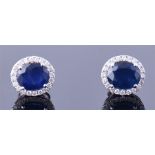 A pair of 18ct white gold, diamond, and sapphire cluster earrings of oval form, each set with a blue
