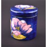 A Moorcroft Magnolia pattern pot and cover decorated with pink magnolia flowers on a blue ground.