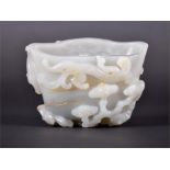 A 19th century Chinese white jade Libation cup crafted from a single large boulder, heavily carved