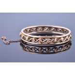 An early 20th century yellow metal openwork hinged bangle  with interwoven design, unmarked, bearing