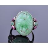 A Chinese white metal, jade, and ruby ring set with an oval carved and pierced jade plaque decorated
