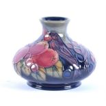 A Moorcroft Finches squat vase decorated with birds and fruit on a green and blue ground.