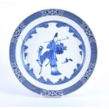 A Chinese blue and white plate decorated with a spotted deer presenting a leaf to a lady carrying