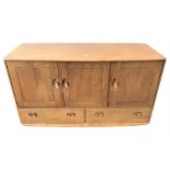 A light Ercol sideboard with three panelled cupboard doors revealing a shelved interior, set above a