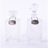 A pair of oak cased glass decanters both lidded and with silver drinks labels around their necks,