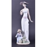 A Lladro figurine of an elegant lady in a hat and sundress she picks flowers with a young child,