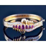 A yellow metal, diamond, and ruby bangle the crossover style mount bezel set with seven graduated