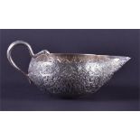 A silver oil pouring vessel with a shallow body and intricate floral and foliate patterning, the