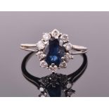 A white metal, diamond, and sapphire cluster ring set with an oval-cut sapphire of approximately 1.