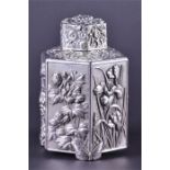 A hexagonal white metal Japanese tea caddy decorated with various plants and blossoms including