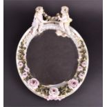 A 20th century Meissen style ceramic mirror of oval form, surmounted with two seated putti holding a