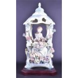 A Lladro ceramic of a young girl  in an ornate pagoda, surrounded by flowers on a wooden base,