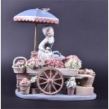 A Lladro figurine of a female flower seller she stands under a parasol, offering her wares out of