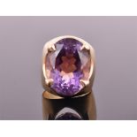 A yellow metal and amethyst cocktail ring set with a large oval cut amethyst in raised stylised claw