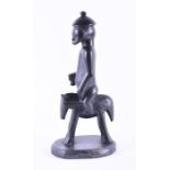 A 20th century ebonised tribal figure a nude male riding a four legged creature, on a wooden base,