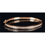 A yellow metal and diamond hinged bangle channel-set with round brilliant cut diamonds of