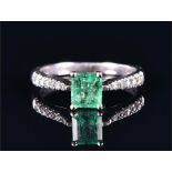 A white metal, diamond, and emerald ring set with an emerald cut emerald of approximately 1.0 carat,