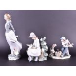 Two Lladro figures to include a woman standing in a breeze together with a Lladro figure of a boy