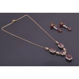 A yellow metal, white stone, and garnet drop pendant necklace set with four clusters of