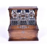 An early 20th century oak and white metal bound tantalus containing three cut glass bottles of