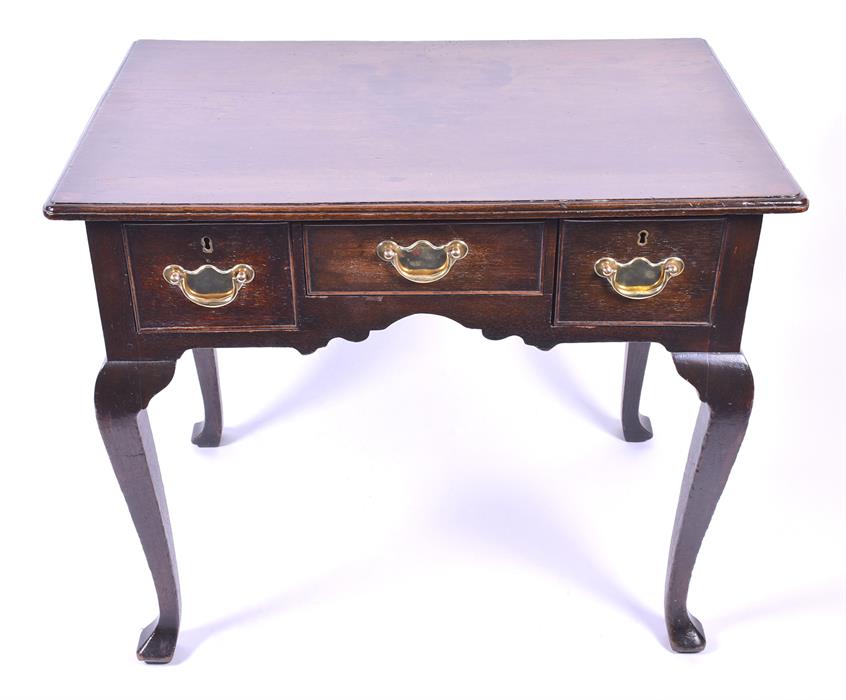 An 18th century oak lowboy the rectangular top with moulded rim, over three small drawers with brass