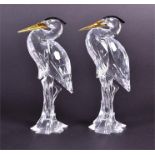 Two Swarovski crystal models of herons with glass eyes, black crests and yellow beaks, approximately