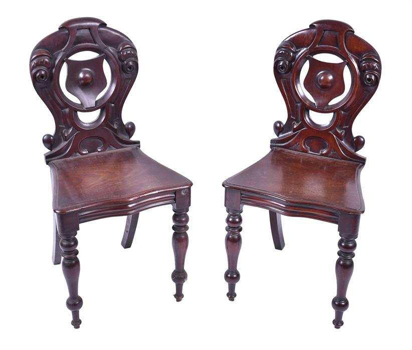 A pair of early 20th century dark wood shield back hall chairs with carved cartouche, turned back